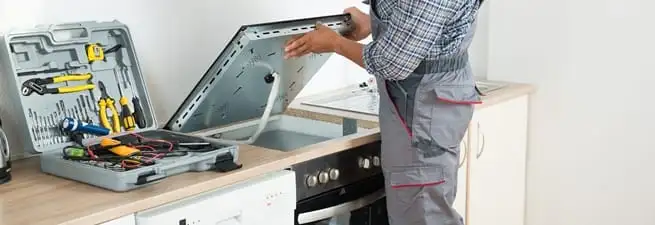 Cooktop repair technician lifting a built-in stovetop for service in Naperville, IL