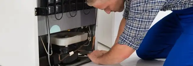 Refrigerator repair technician servicing the compressor and condenser area in Naperville, IL