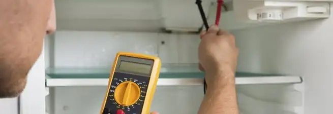 Refrigerator repair technician testing electrical components with a multimeter in Naperville, IL